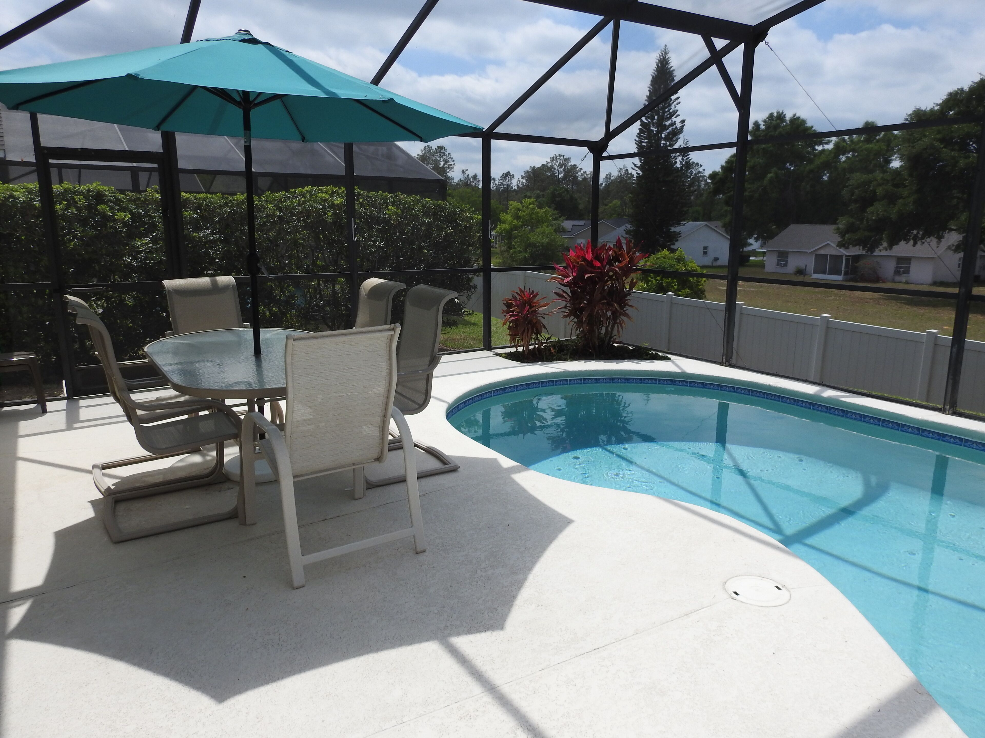 A covered outdoor area with a pool, a table with chairs, and a patio umbrella.