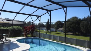 Piscina com borda curva, rodeada por um terraço coberto com cadeiras e uma mesa.