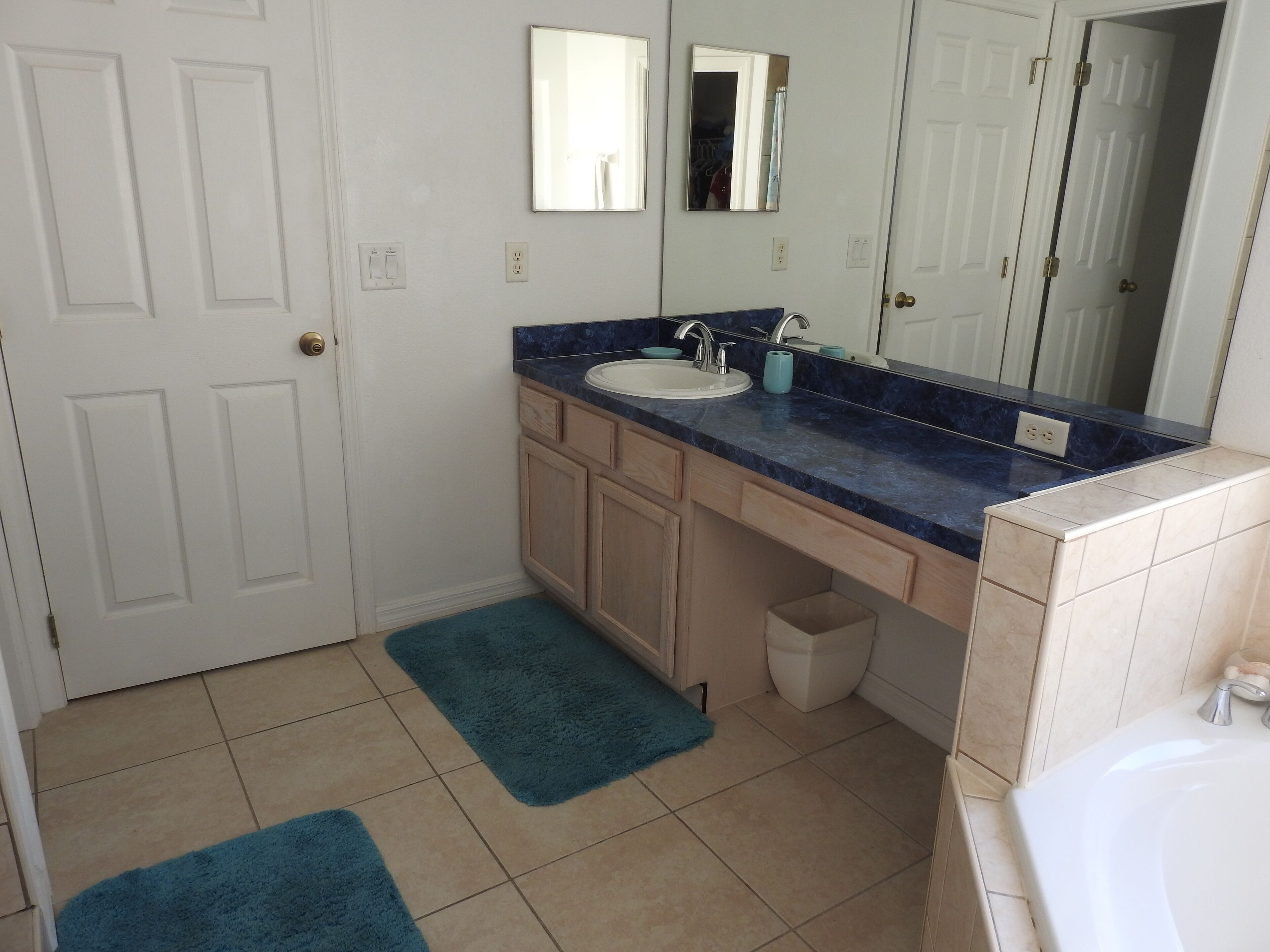A bathroom with a white door, a sink with a blue countertop, a mirror above the sink, and a white bathtub.