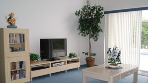 Sala de estar com televisão, estante de livros e plantas em vasos.