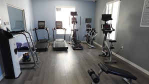 Uma academia com esteiras, elípticos e um banco de musculação.
