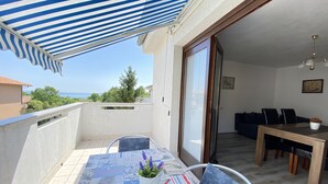 A balcony with a striped awning, a dining table with chairs, and a view of the sea.