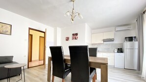 A modern kitchen with white cabinets, a microwave, and a coffee maker. There is a dining table with chairs and a sofa in the living area.