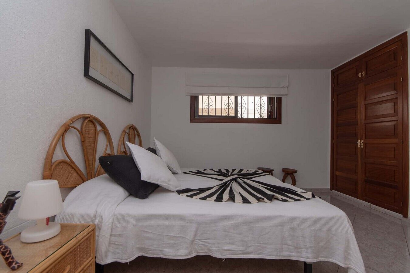 A bedroom with a bed, a bedside table, a lamp, a window with a curtain, and a wardrobe.