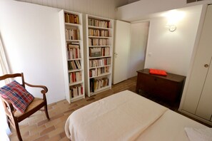 A bedroom with a bed, a chair with a plaid cushion, a wooden dresser, and a bookshelf filled with books.