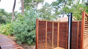 Une terrasse en bois, agrémentée d’un écran pour plus d’intimité et d’un poteau vertical, le tout entouré de verdure.
