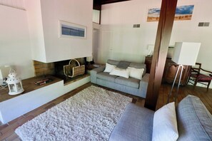 Ein Wohnzimmer mit grauem Sofa, einem weißen Teppich, einem Kamin und einem Gemälde an der Wand.