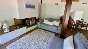 Un salon chaleureux avec une cheminée, un canapé gris, un tapis blanc et un plancher en bois.