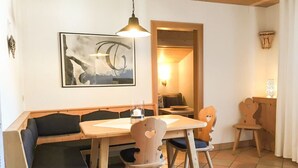 A cozy dining area with wooden furniture, a table, and chairs. There is a painting on the wall and a hanging light fixture.
