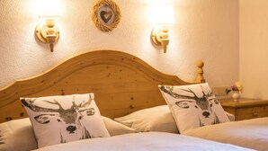 A wooden bed with two pillows featuring deer designs, a wall-mounted light fixture, and a small bedside table with a vase of flowers.