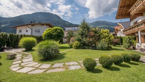 A well-maintained garden with stone pathways, neatly trimmed bushes, and a view of mountains in the background.