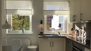 A modern kitchen with white cabinets, a built-in oven, and a window with a view of buildings and trees.