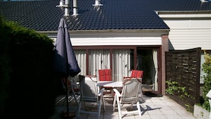 Un patio con mesa y sillas, un área techada y una casa con tejado de tejas y chimeneas.