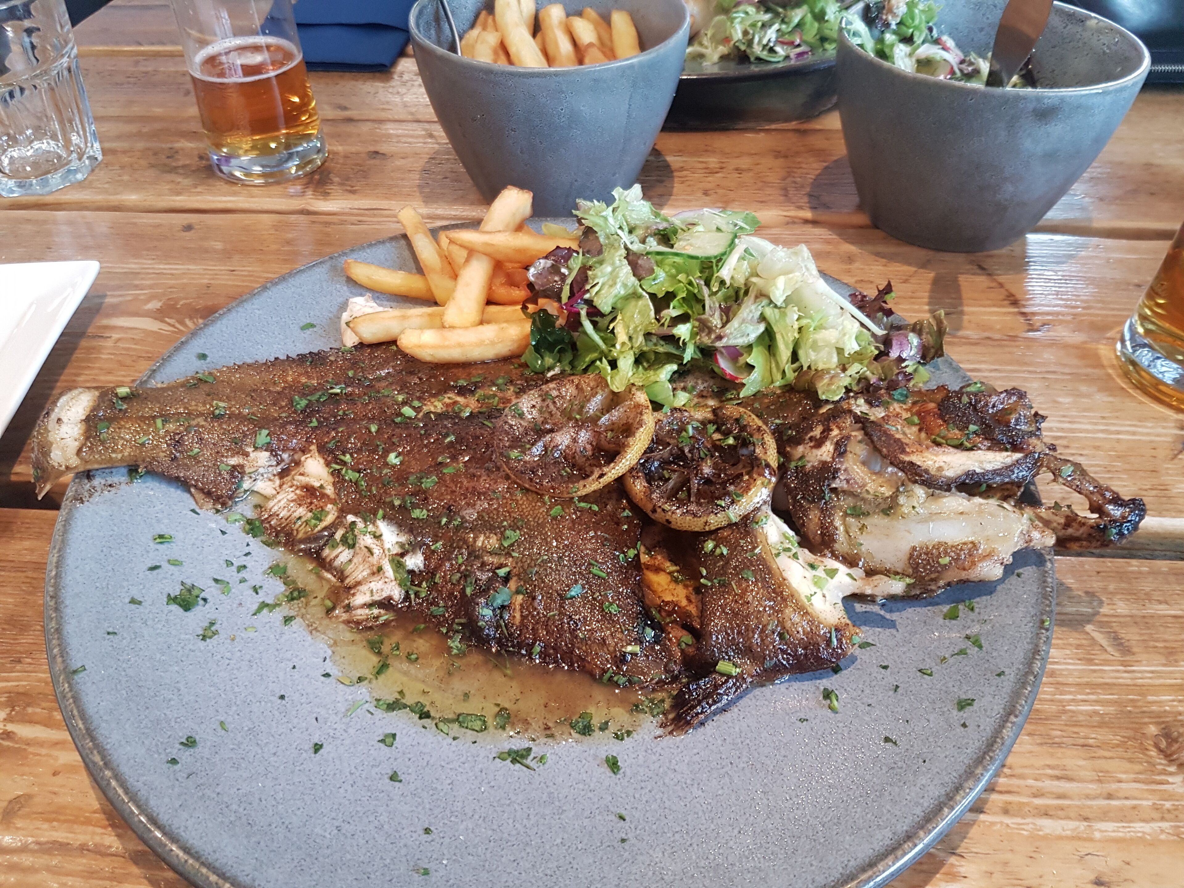 A plate of grilled fish with fries and salad on a wooden table.