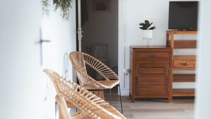 A room with two wicker chairs, a wooden cabinet, and a television on a stand. - BUNGALOW T3 PITAYA (Saint-Paul)