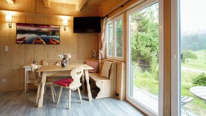 Un interior de madera con una mesa de comedor, sillas, un sofá y un ventanal con vistas a la vegetación y una carretera.