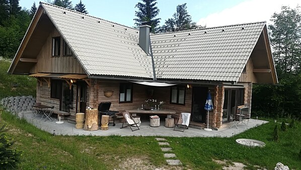 Une cabane en rondins dotée d’un patio couvert, de meubles d’extérieur et d’un barbecue.