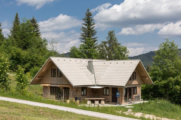 A rustic cabin with a sloped roof, wooden exterior, and a small porch with a table and chairs.