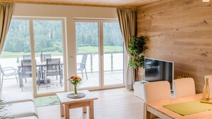 Un salon moderne avec un plancher en bois, un canapé, une table à manger agrémentée d’un vase de fleurs, un téléviseur à écran plat et un balcon avec des meubles d’extérieur.