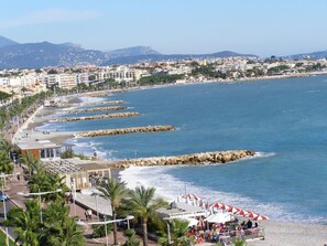 Un paysage urbain côtier avec une plage, des brise-lames rocheux et une rangée de bâtiments le long de la côte.