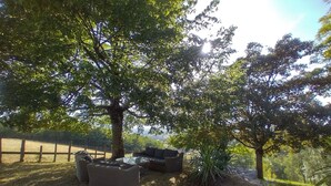 Een terras met rieten meubels en een glazen tafel, omgeven door bomen en een houten hek.