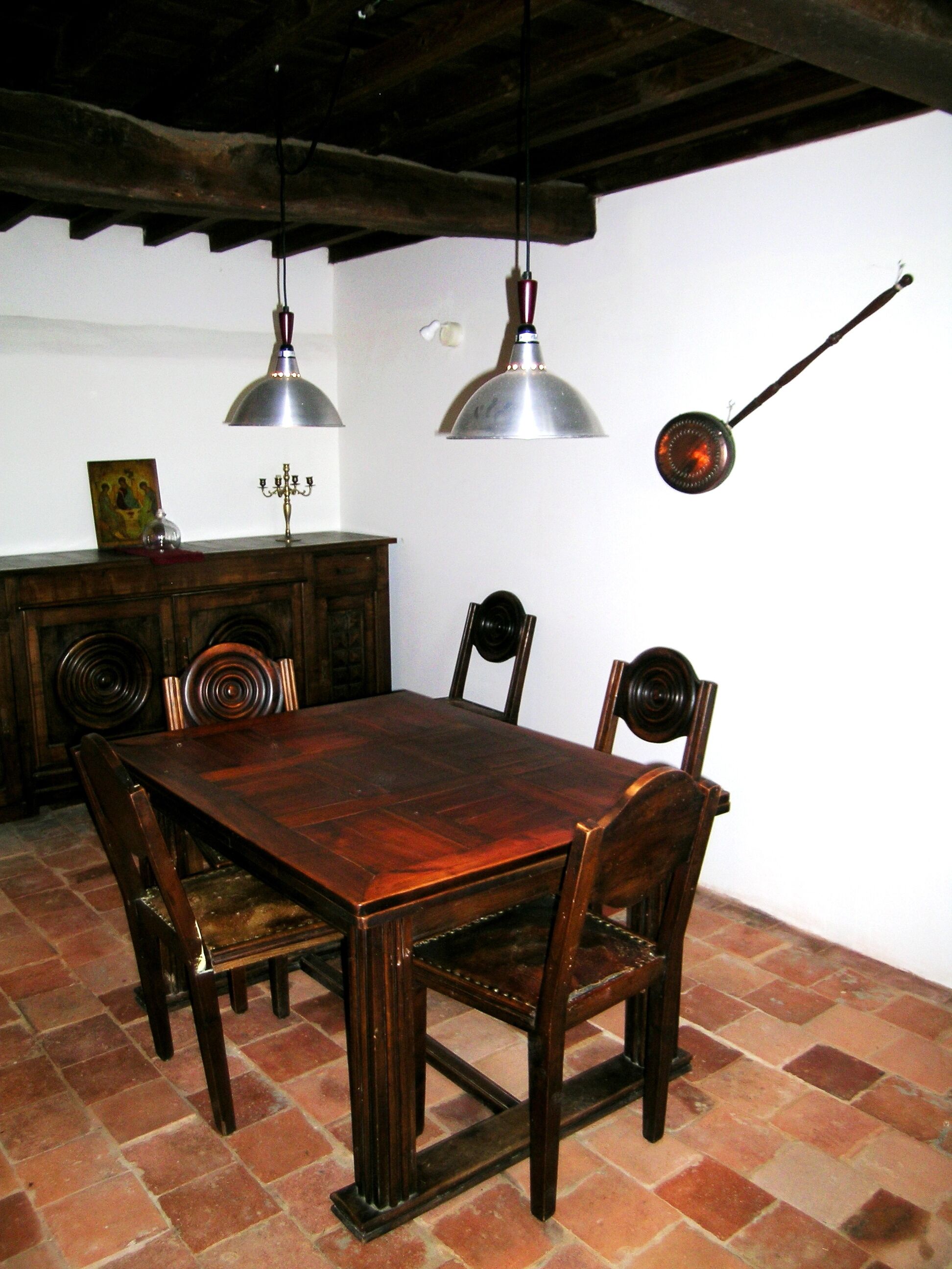 Een eetgedeelte met een houten tafel en stoelen, twee hanglampen, een aan de muur bevestigde spiegel en een decoratieve kandelaar.