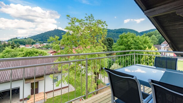 A balcony with a view of a green landscape, houses, and mountains.