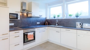 A modern kitchen with white cabinets, a built-in oven, a microwave, a sink, and a window with potted plants.
