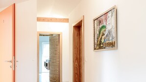 A hallway with a wooden floor, a painting on the wall, and a door on the left.
