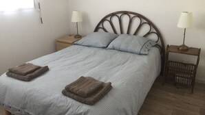Ein Bett mit gestreifter Bettdecke, zwei Kissen und zwei gefaltete Handtücher. Zwei Nachttische mit Lampen und eine Wanddekoration befinden sich über dem Bett.
