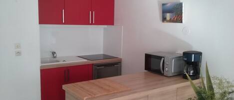 A compact kitchen with red cabinets, a sink, a dishwasher, a microwave, and a coffee maker.