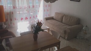 Ein Wohnzimmer mit einem beigefarbenen Sofa, einem Couchtisch aus Holz mit einer Pflanze und einem Essbereich mit Tisch und Stühlen.