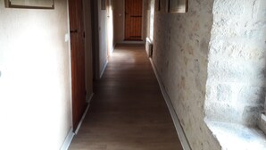 Un couloir étroit, doté d’un plancher en bois et de murs en pierre, qui mène à une porte en bois au bout.