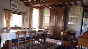 Un espace repas avec une longue table en bois, des chaises et une nappe à motifs. On y trouve également des meubles en bois et un lustre.