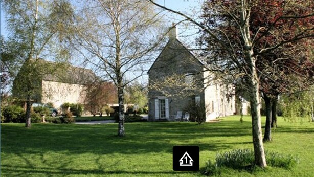 Un bâtiment en pierre doté d’un toit à deux versants, entouré d’une pelouse bien entretenue et d’arbres.