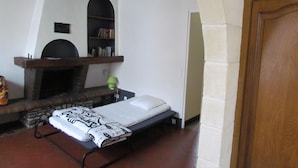 Een slaapkamer met een bed, een open haard, een plank met boeken en een houten plafond.