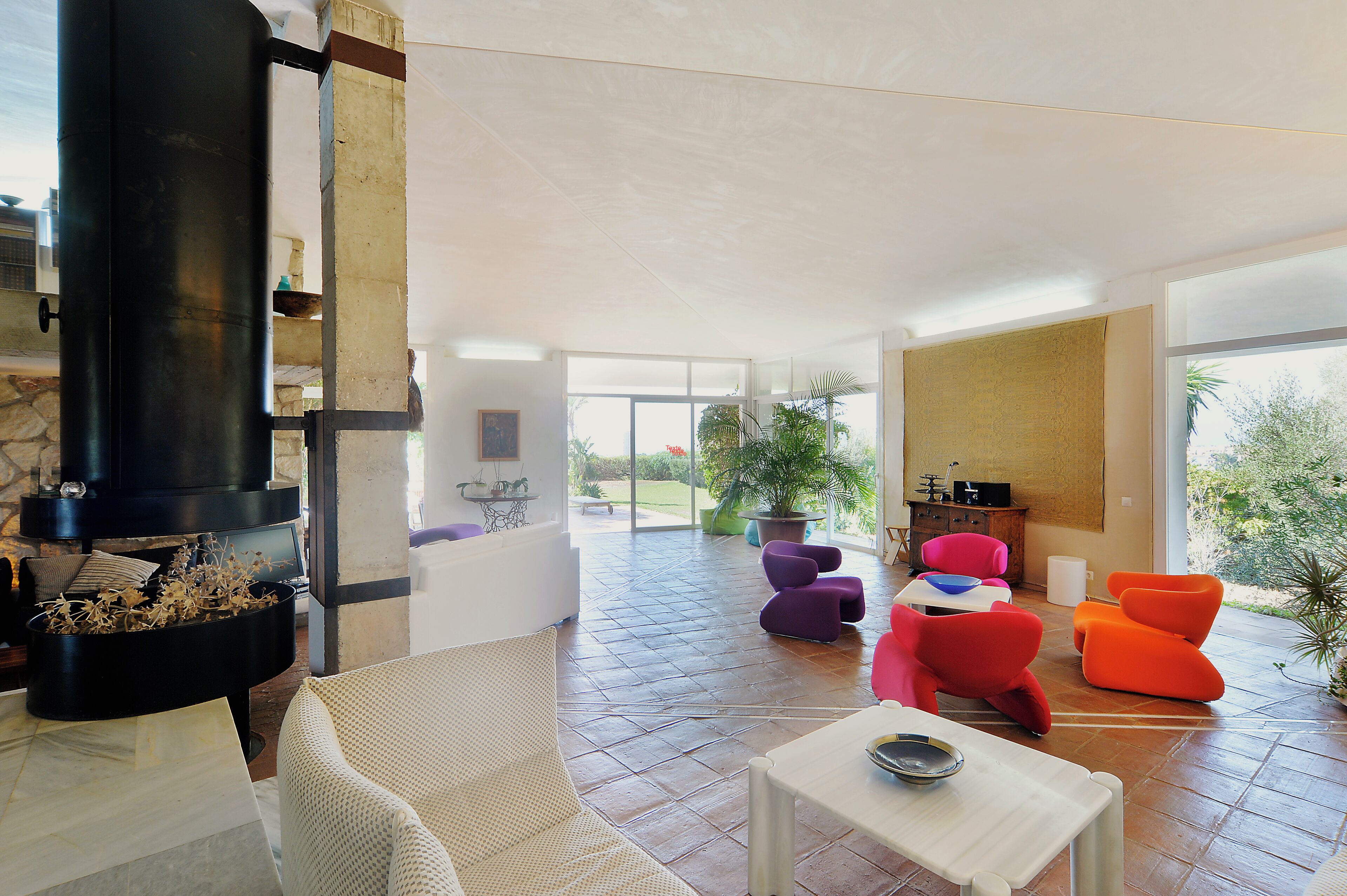 A spacious living area with a fireplace, colorful chairs, and a view of the outdoors.