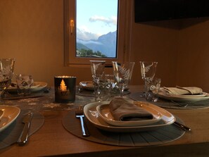 A dining table set with plates, cutlery, and glassware, with a candle and a view of mountains through a window. - Appart ski aux pieds 8 pers : 3ch 2sdb - Sheets-Linen-Household-Wifi-Parking-TV's (Les Deux alpes - Mont de Lans)