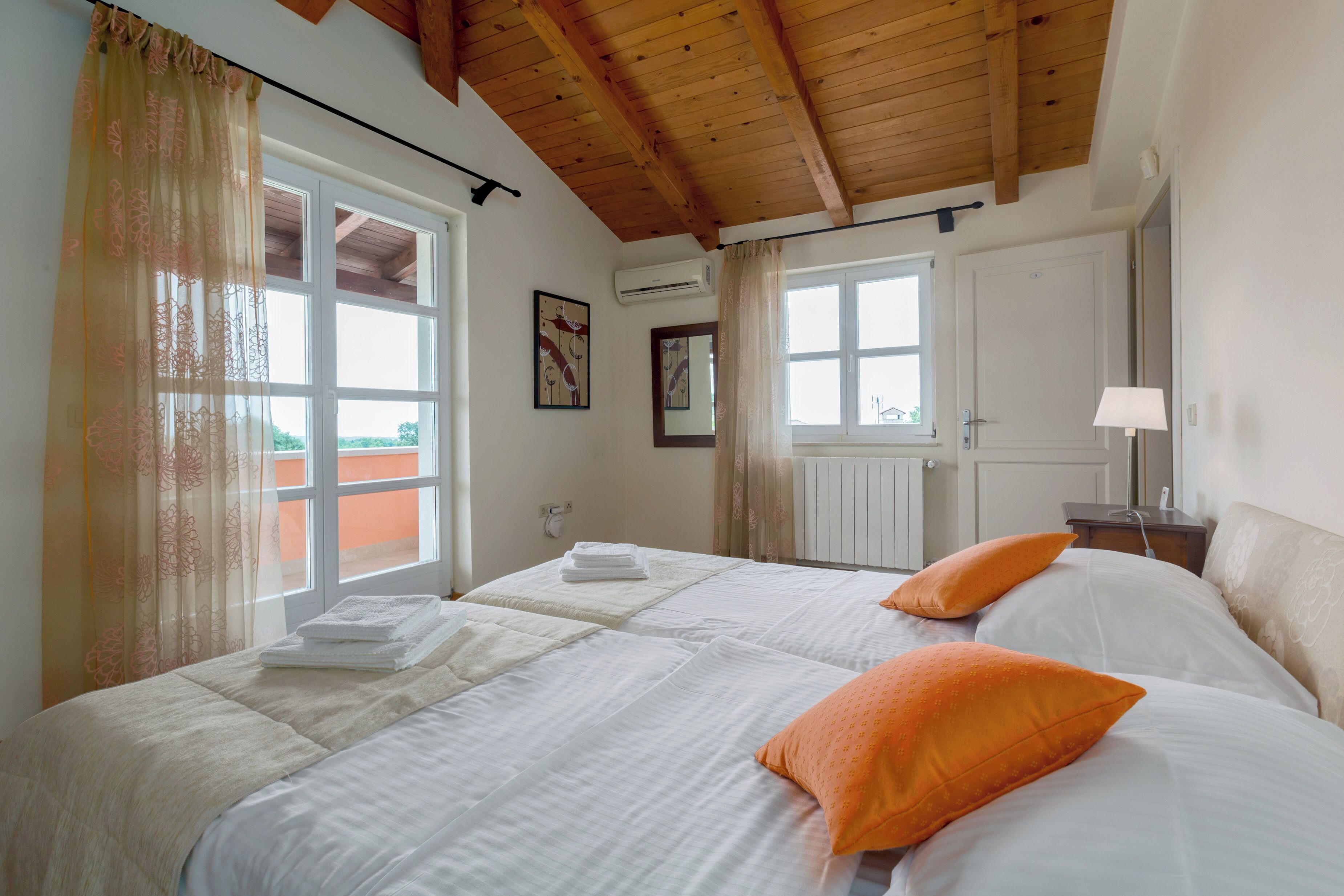 A room with two beds, a wooden ceiling, and a window with curtains.