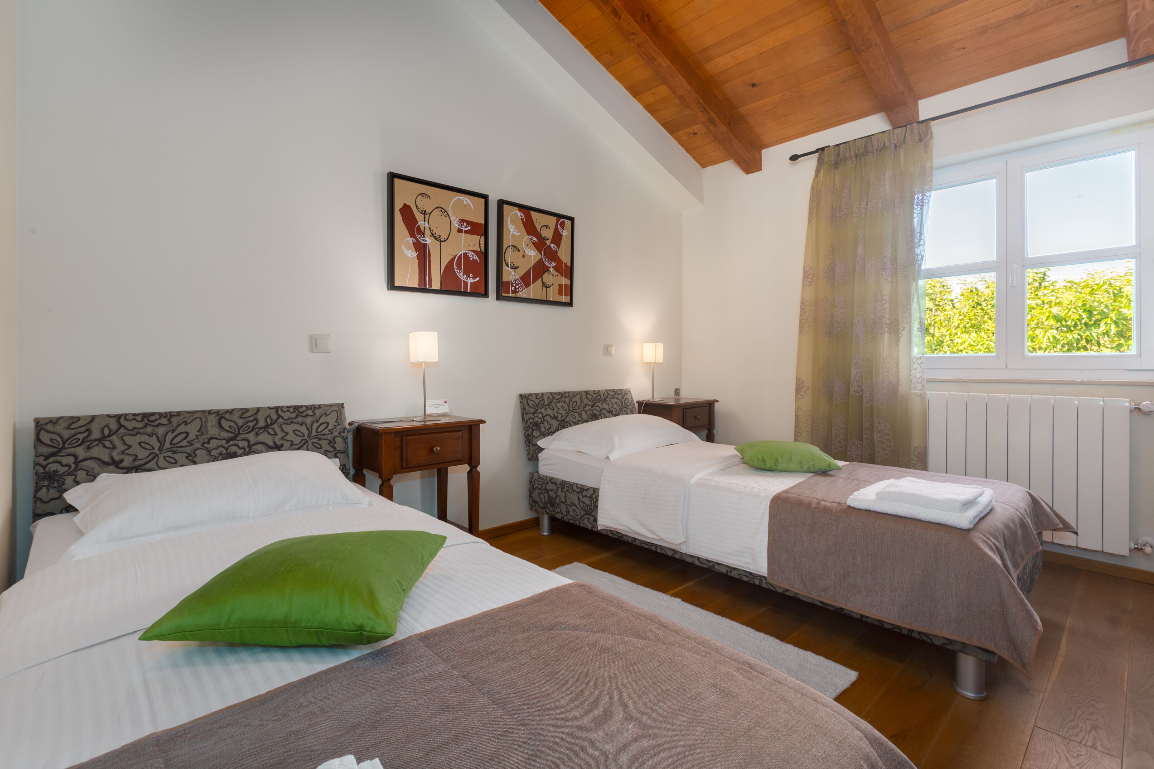 A hotel room with two beds, a window with curtains, a radiator, and two wall-mounted lamps.
