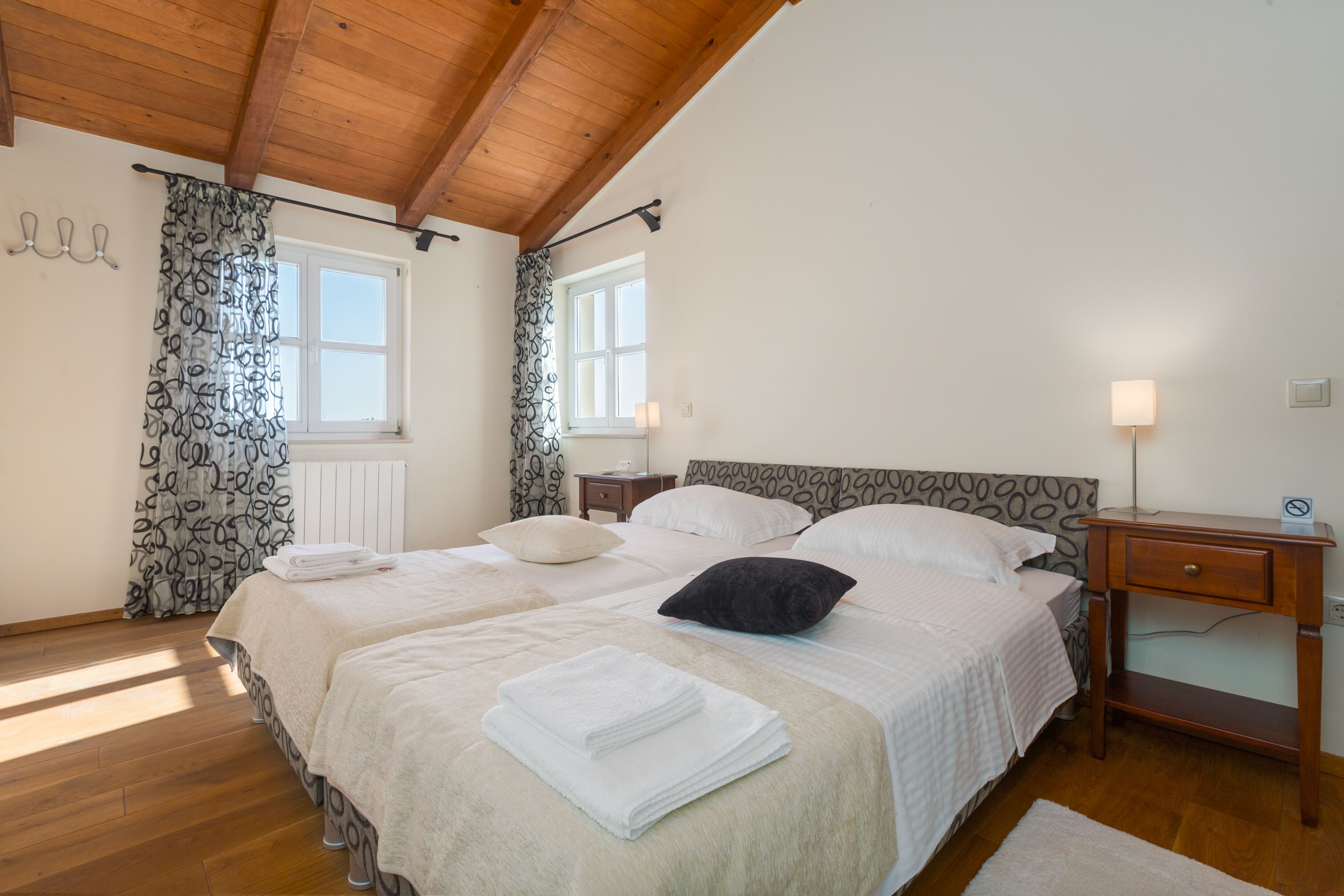 Camera da letto con due letti, pavimento in legno, travi a vista al soffitto e comodino con lampada.