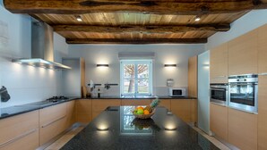 Eine moderne Küche mit Kochinsel, Edelstahlgeräten, Holzschränken und einem großen Fenster.
