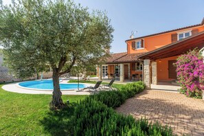 Ein Haus mit Schwimmbad, Terrasse mit Stühlen und Garten.