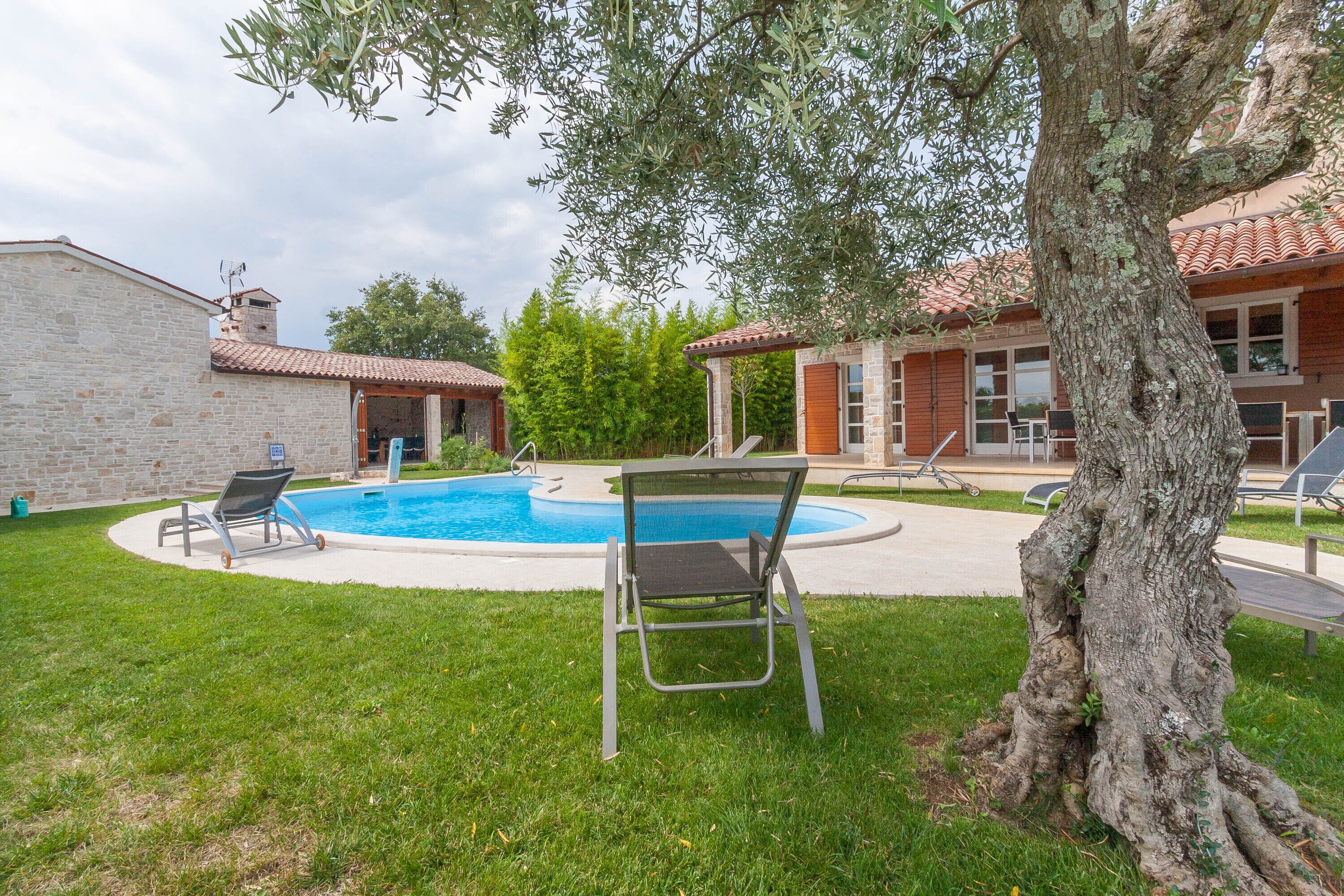 A swimming pool with two lounge chairs, a stone building, and a tree in a backyard setting.