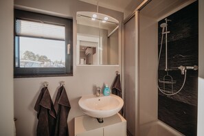 Un baño con lavamanos blanco, espejo y ducha.