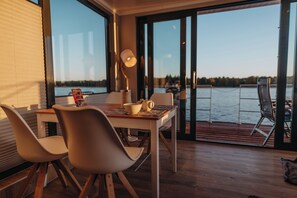 Un comedor con mesa, sillas y lámpara. La habitación tiene ventanas amplias con vistas al agua.