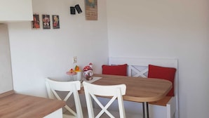 A dining area with a wooden table and white chairs, a small side table with toys, and a wall with framed pictures.