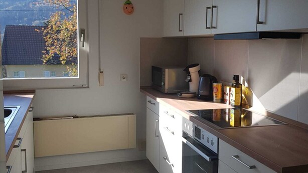 A modern kitchen with white cabinets, a large window, and a view of a house and trees.