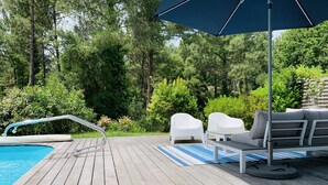 A wooden deck with a pool, white lounge chairs, and a blue umbrella. - BRIGHT VILLA WITH POOL (Moliets-et-Maa)