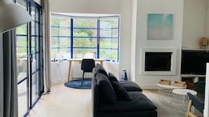 A modern living room with a black sofa, a TV, and a large window with blue frames. - BRIGHT VILLA WITH POOL (Moliets-et-Maa)